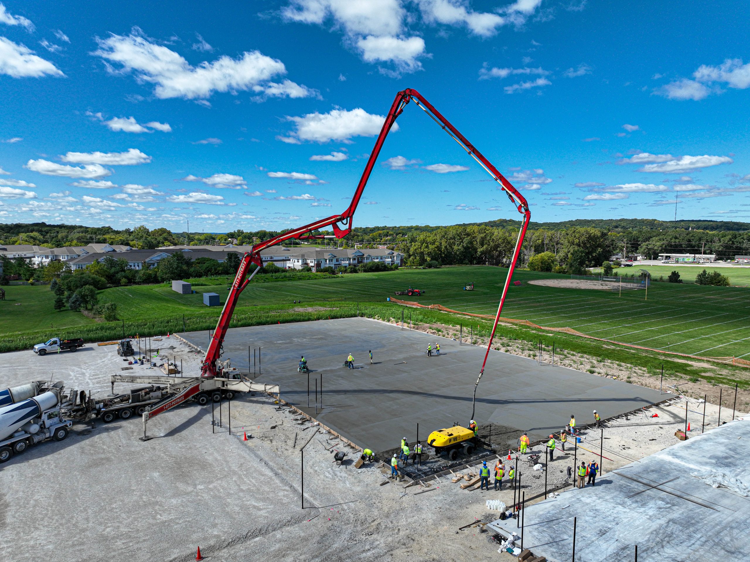 Aerial view showing group of workers leveling Kettle Moraine Tennis Courts, with Moraine High School field in the background