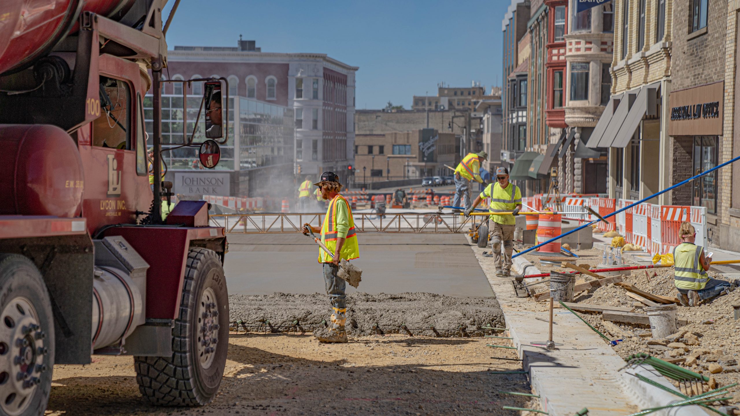 Wide shot of a group of construction workers leveling concrete with a concrete truck in the foreground