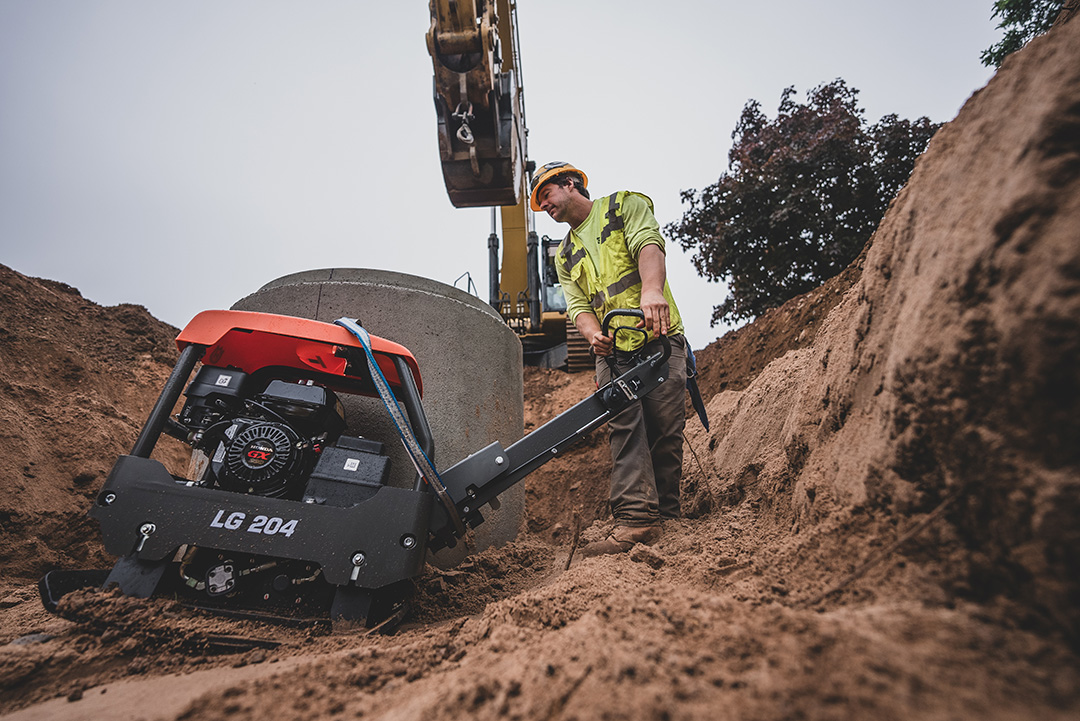 Close up excavation in progress for the Ishpeming sewer project with man in the foreground and excavator in the background
